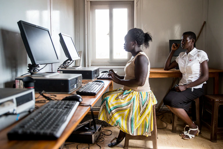 2 woman sitting behind a desk and a computer