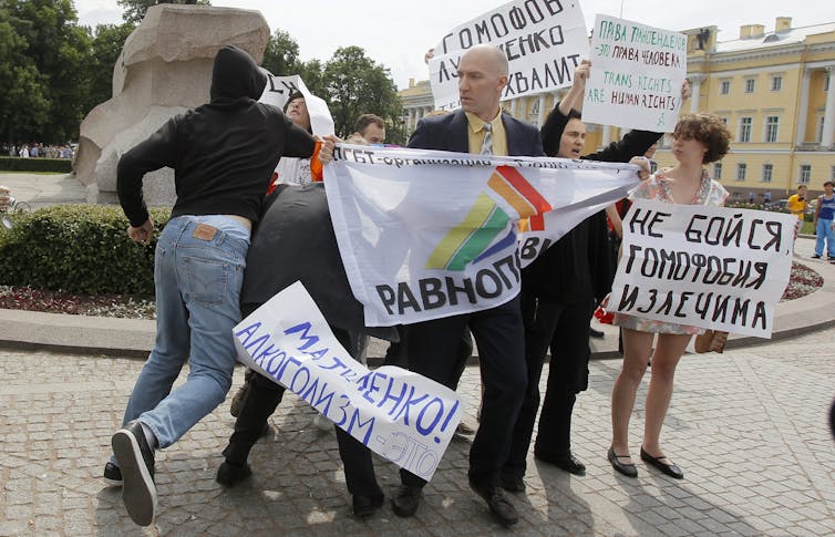 A man in a black hoodie punches a gay rights activist who stands among other activists holding signs that promote tolerance.