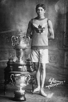 A black and white photo of a man standing beside sports trophies.