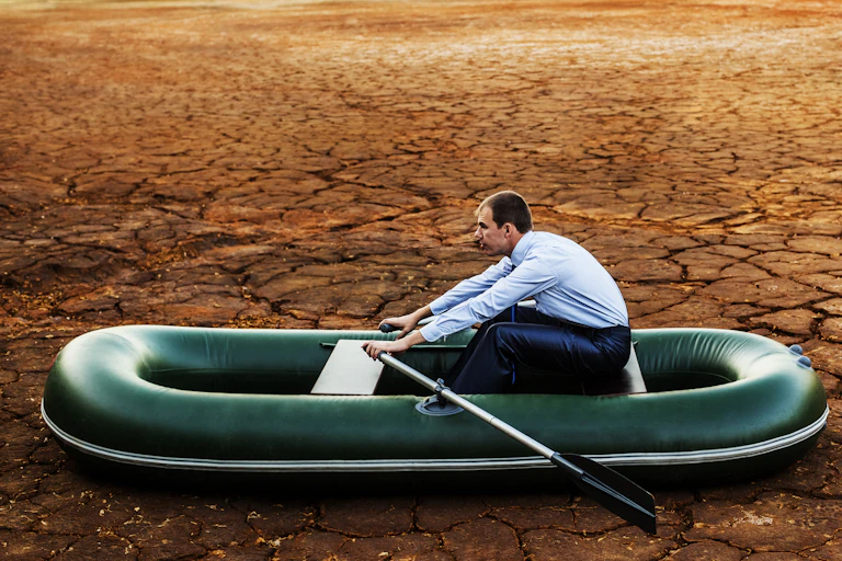 Man on inflatable rowing boat on dried ground