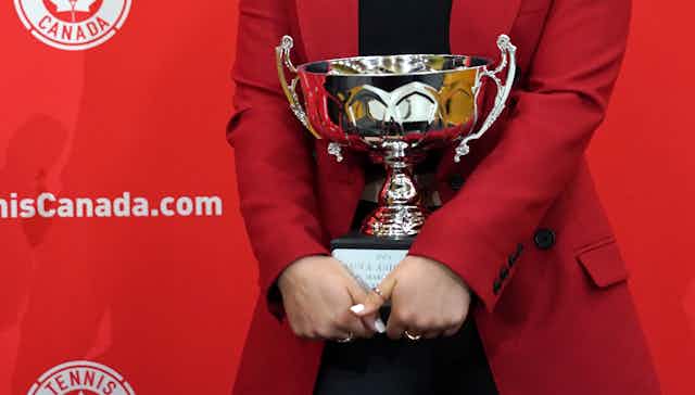 A silver trophy being held by a woman wearing a red jacket.