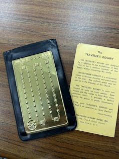 A flat piece of metal that works as a rosary, placed next to a yellowed sheet explaining how to use the Traveler's Rosary.