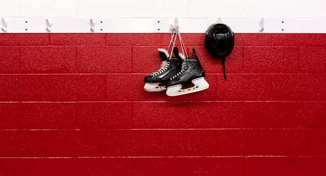 A pair of black hockey skates hang on a hook on a red and white wall.