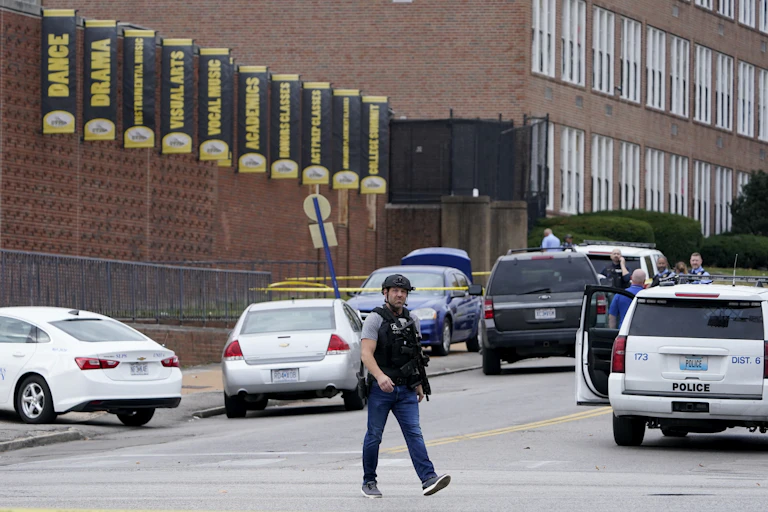 A man in body armor and helmet walks outside the front of a school building.