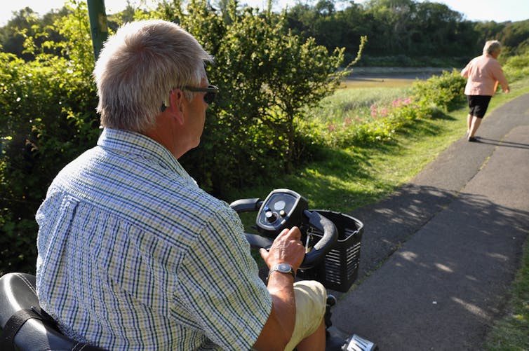 older man on mobility scooter behind woman walking