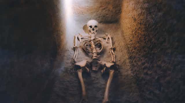 A skeleton is shown lying in a dimly-lit grave 