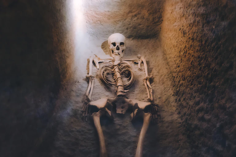 A skeleton is shown lying in a dimly-lit grave