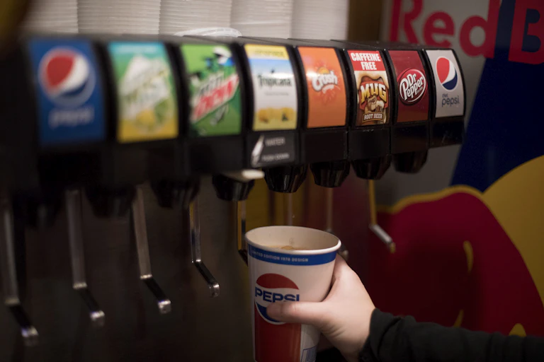 A soda fountain dispenser with eight choices, and a hand holding a paper Pepsi cup under one of the nozzles.