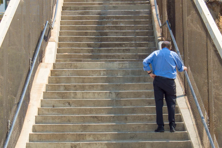 Older man pauses for breath while climbing a long flight ofstairs