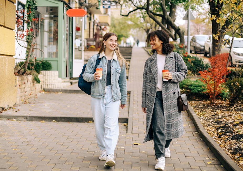 Two young women go for a walk in the city with cups of coffee.
