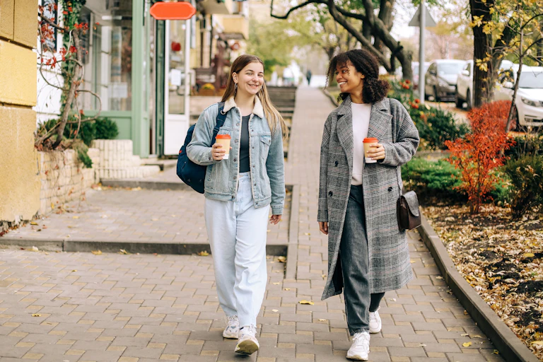 Two young women go for a walk in the city with cups of coffee.