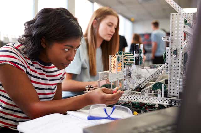 Two girls building model out of metal pieces