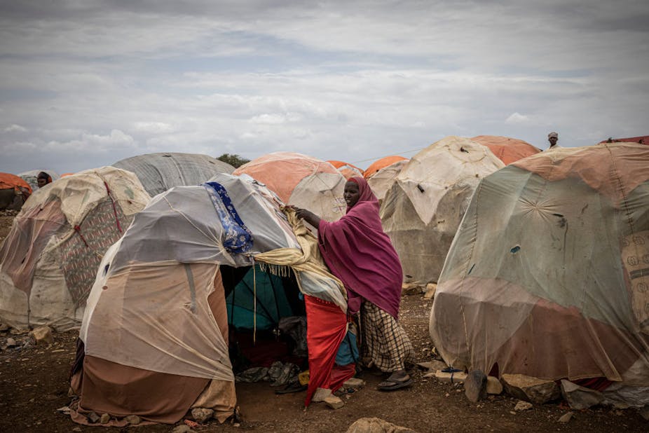 A woman adjusting the sides of a makeshift cloth tent next to several similar structures.