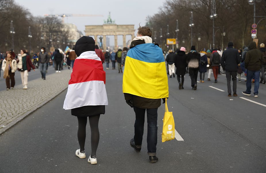 Two protestors, one wrapped in the Belarusian opposition flag and the other in the Ukrainian, walk side by side