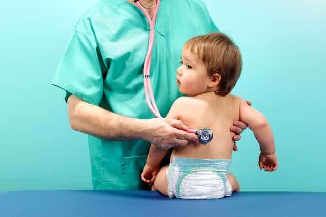 A doctor holding a stethoscope to a baby's back.
