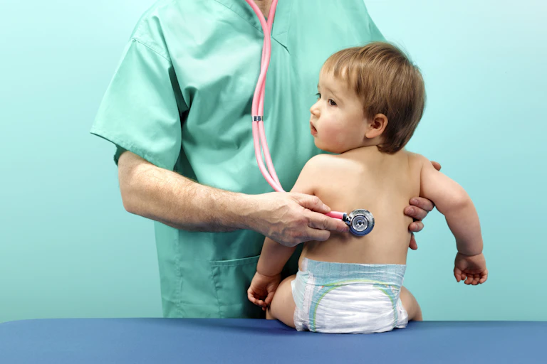 A doctor holding a stethoscope to a baby's back.