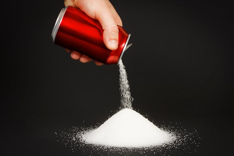 A hand pouring sugar out of a soda can