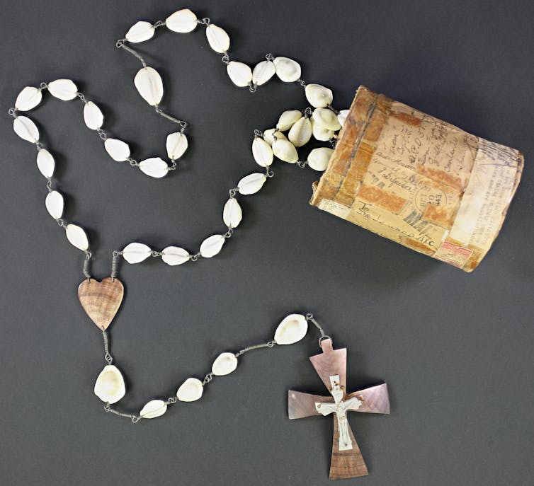 A string of beads made of cowrie shells, with a cross on one end