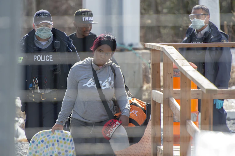 A Black woman lugging her belongings stares into the camera as she's photographed crossing the Canada-U.S. border.