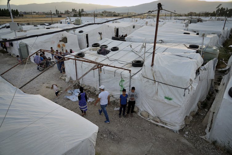People walk by an arid compound crammed with white tents.