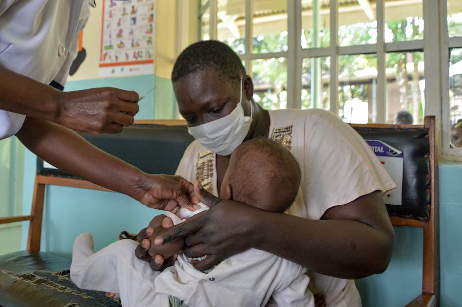 Woman holding a child as a clinical officer gets ready to inject a vaccine. 