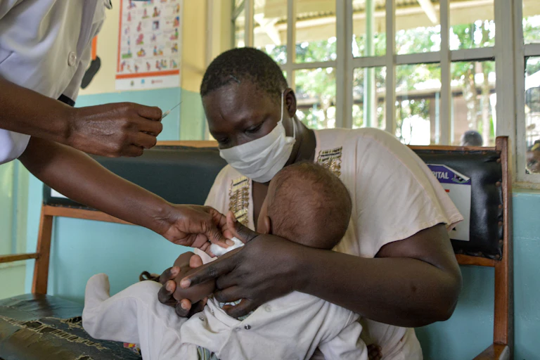 Woman holding a child as a clinical officer gets ready to inject a vaccine.