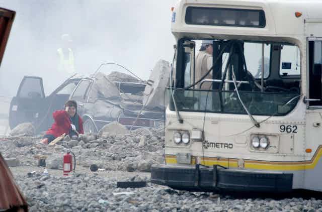 A woman holds her head as she lies in the rubble caused by the explosionof a fake 'dirty bomb'. A wrecked bus sits nearby.