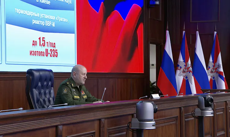 Igor Kirillov, head of the Russian Radiation, Chemical, and Biological Protection Forces deliveries his speech in front of TV screen read as ‘Uranium ores U-238’.