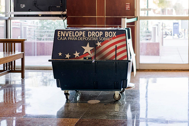 A large blue box on wheels has an American flag and says 'Envelope drop box' in what appears to be an indoor space.