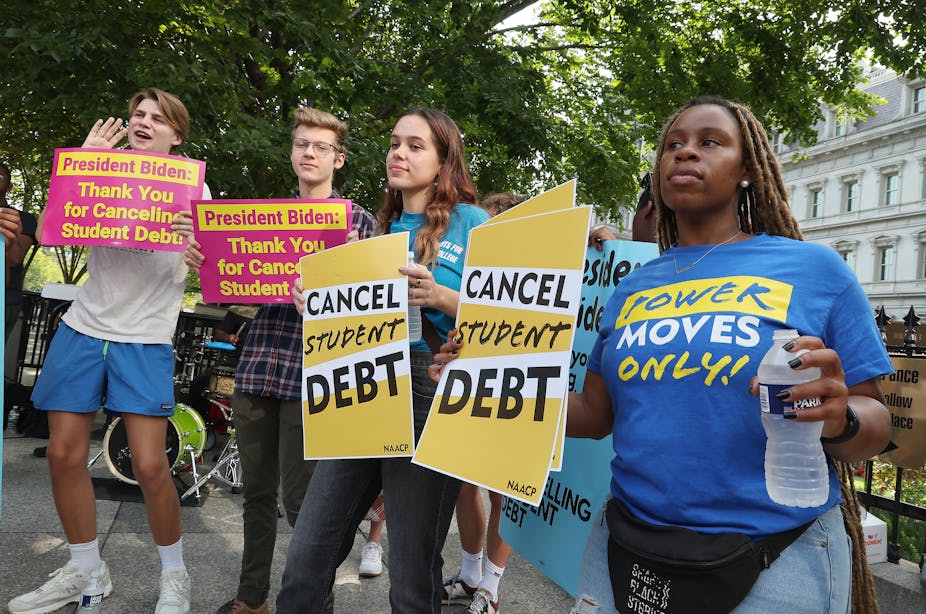 Student loan borrowers hold placards saying "cancel student debt,' thank you for cancelling debt,' and 'power  moves only.'