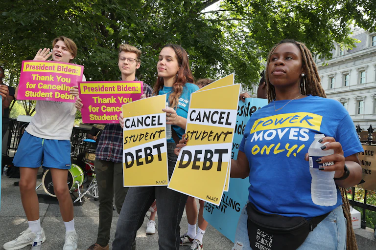 Student loan borrowers hold placards saying "cancel student debt,' thank you for cancelling debt,' and 'power moves only.'