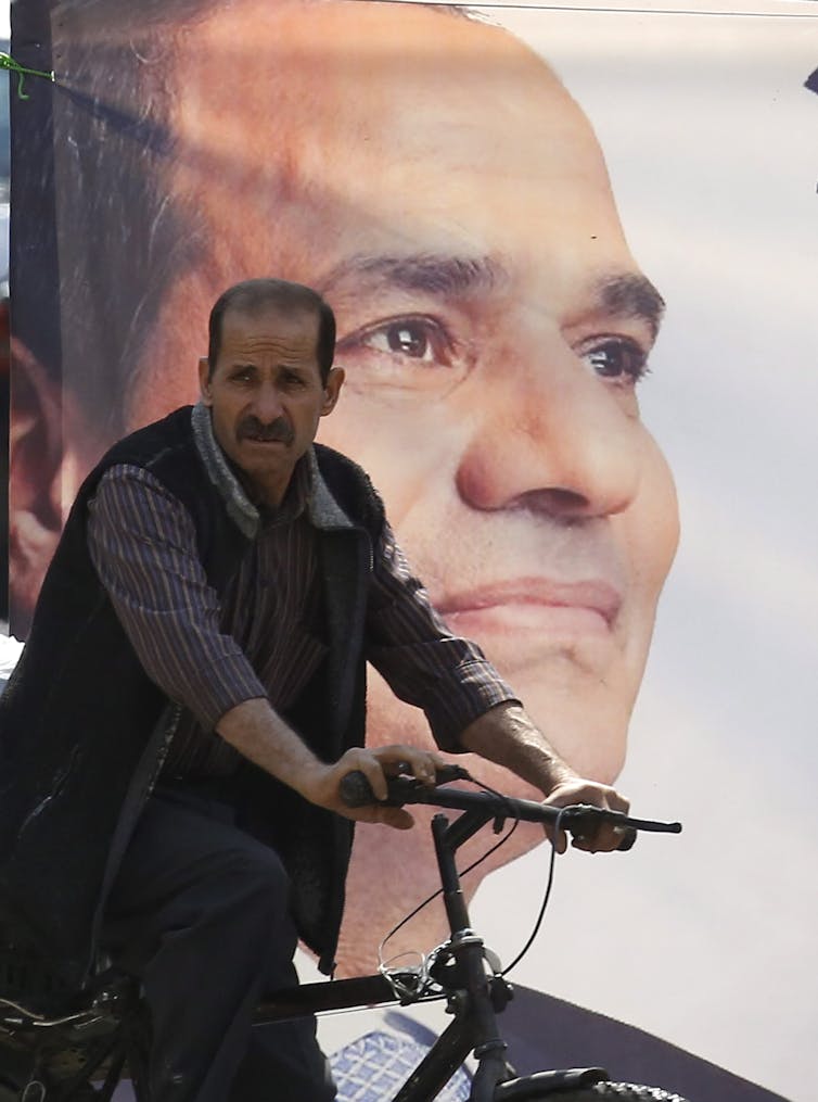 Un homme à vélo, devant une affiche électorale