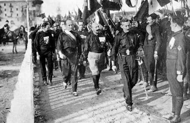 Mussolini and black shirt fascists marching with Italian flags. 