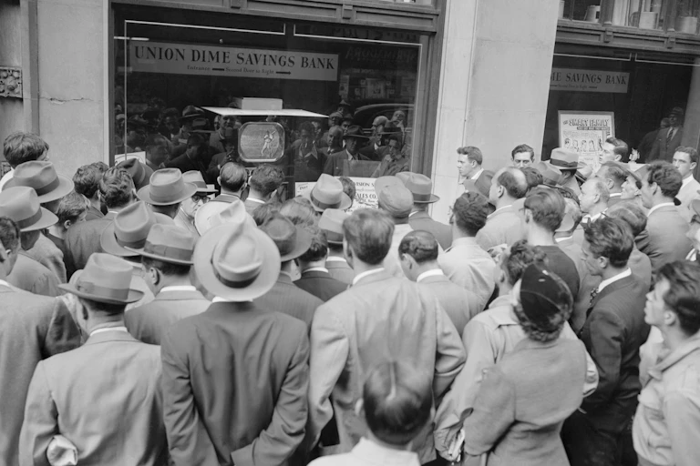 Black and white photo of crowd gathered before a TV airing a baseball game.