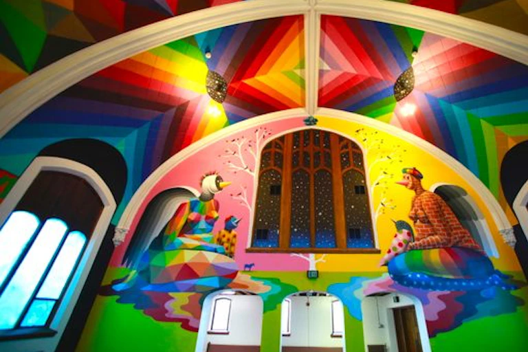 A church with a flamboyant technicolor interior, with a mural on the wall showing two figures smoking weed.