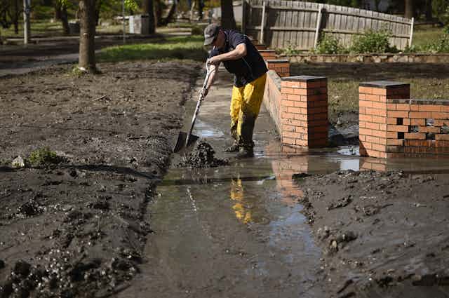 A man cleans up a footpath covered in mud after floodwaters recede
