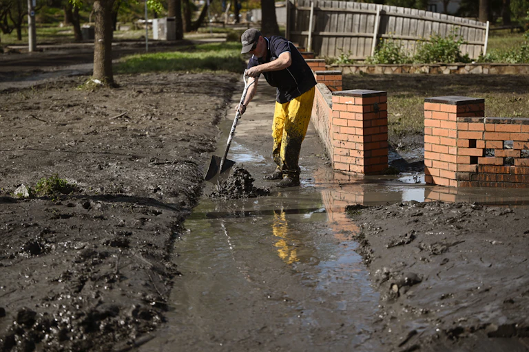 A man cleans up a footpath covered in mud after floodwaters recede