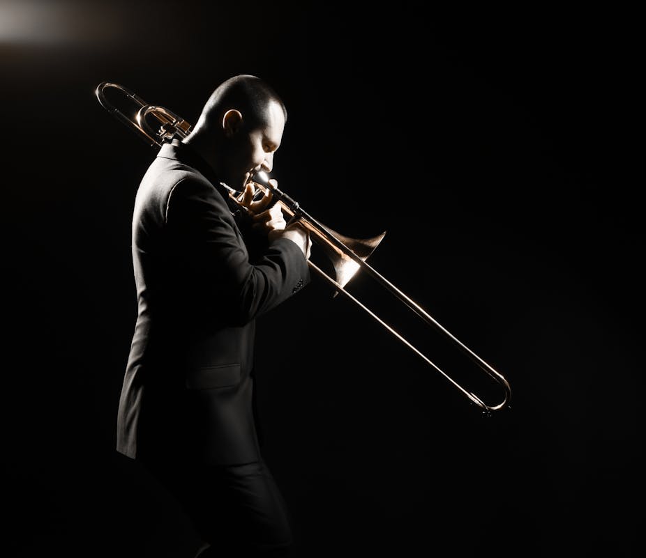 Older man playing the trombone on a darkened stage