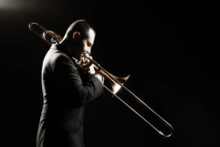 Older man playing the trombone on a darkened stage