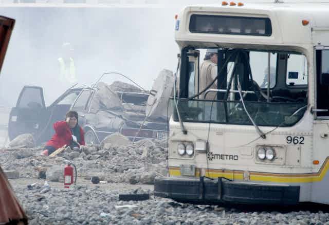 Una mujer entre escombros junto a un autobús blanco.