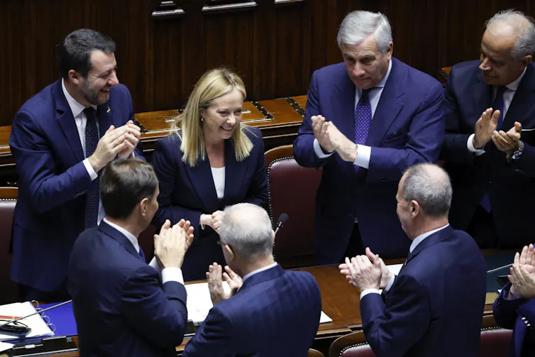 Giorgia Meloni in parliament, surrounded by people clapping.