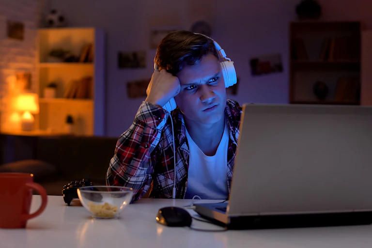 A young man wearing headphones looks angrily at a computer screen