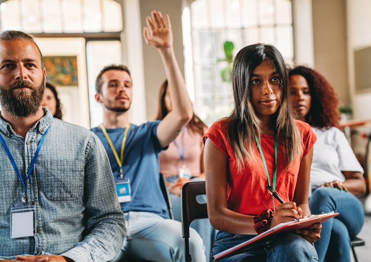 A group of people sitting in chairs with one person raising their hand.