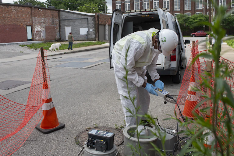 man in protective gear samples wastewater at the street level