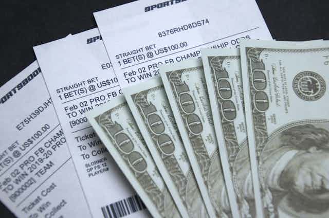 100 dollar bills on top of sports betting slips.