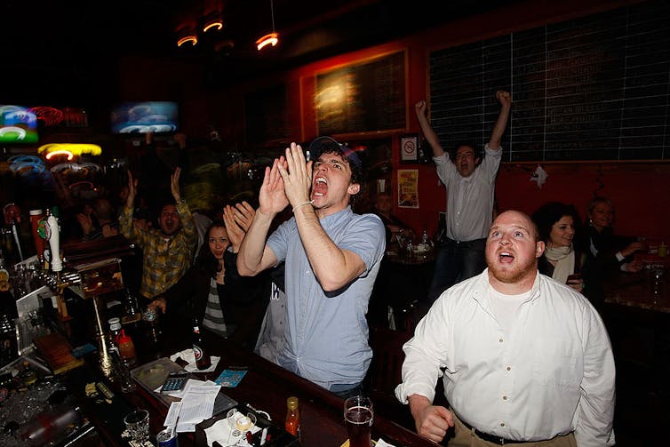 Bar patrons celebrate while watching a baseball game.