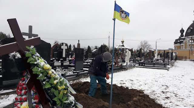 A Ukrainian digs a grave in snowy ground.