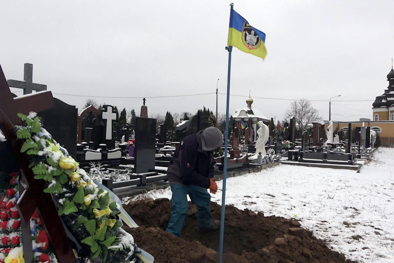 A Ukrainian digs a grave in snowy ground.