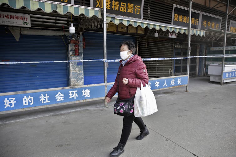 A woman wearing a mask walks past the closed Huanan Seafood Wholesale Market in 2020.