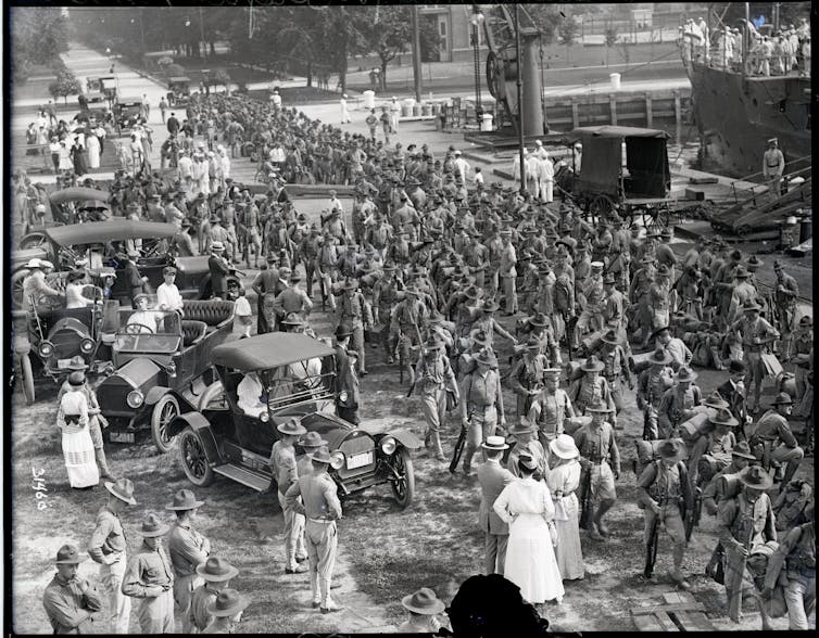 Members of the armed forces march down a city street in the early 20th century.